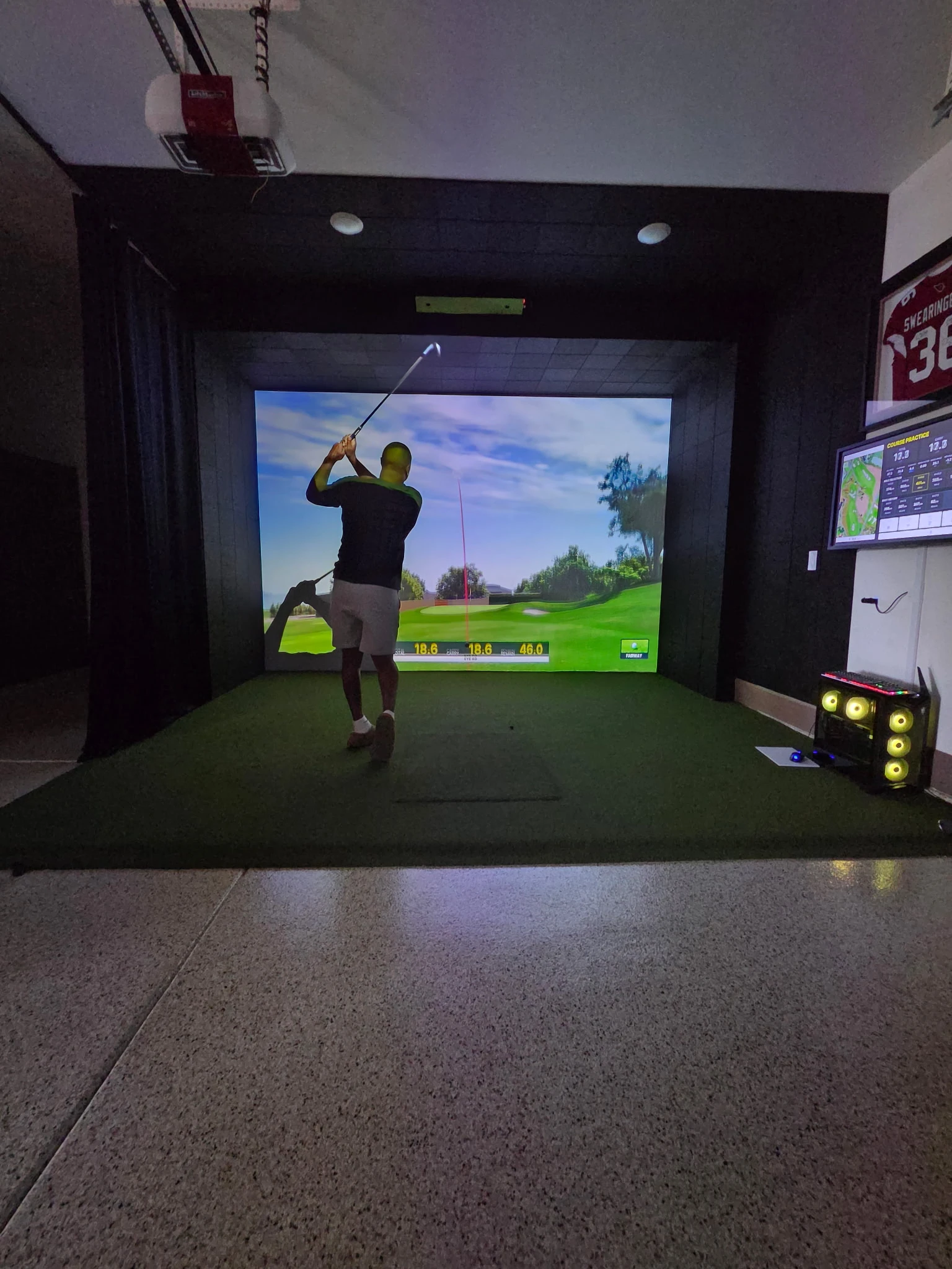 Golfer playing in a custom garage golf simulator with padded surround and overhead equipment