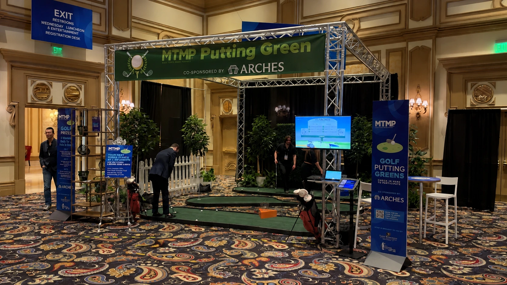 Branded indoor event putting-green installation with multiple greens, participant area and surrounding event signage
