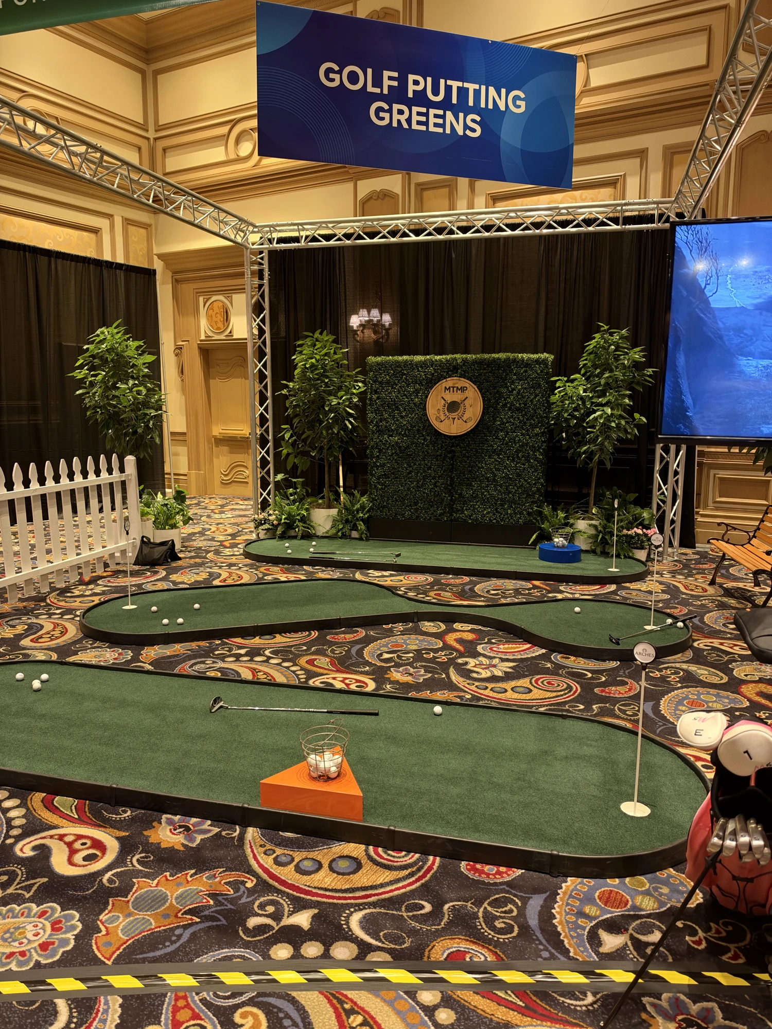 Closer view of several shaped putting greens with cups, flags and putters at an indoor event